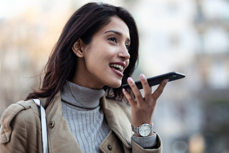 Pretty young woman using voice recognition system on her smartphone while standing in the street.