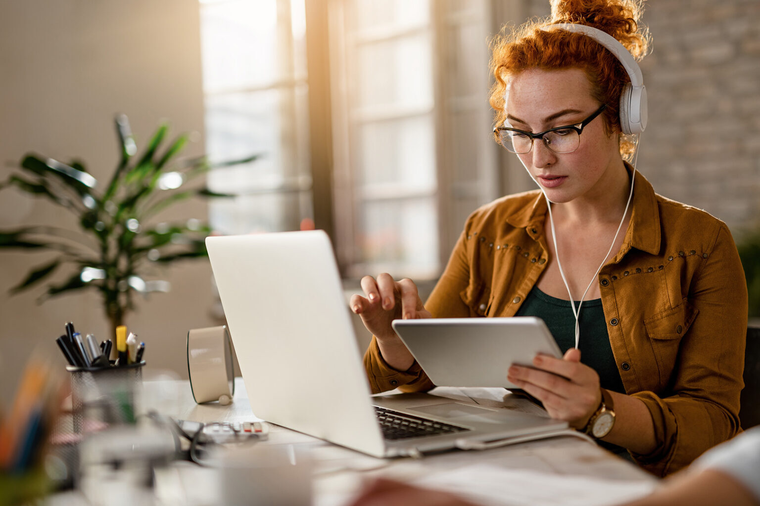 red-haired woman with headphones uses a tablet