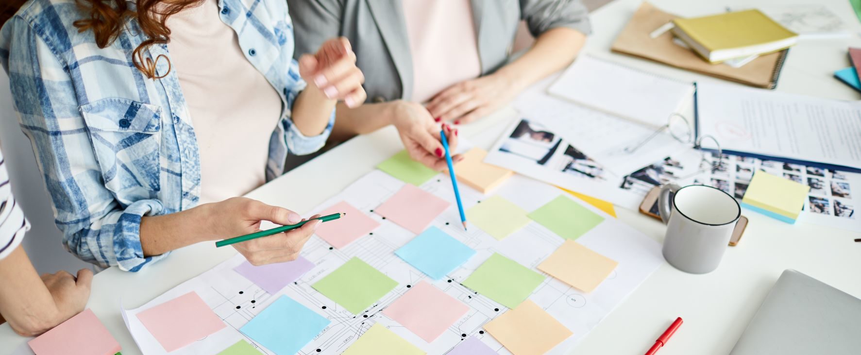 Professionals collaborating over a table that has multicolored stickie notes depicting a mapped process