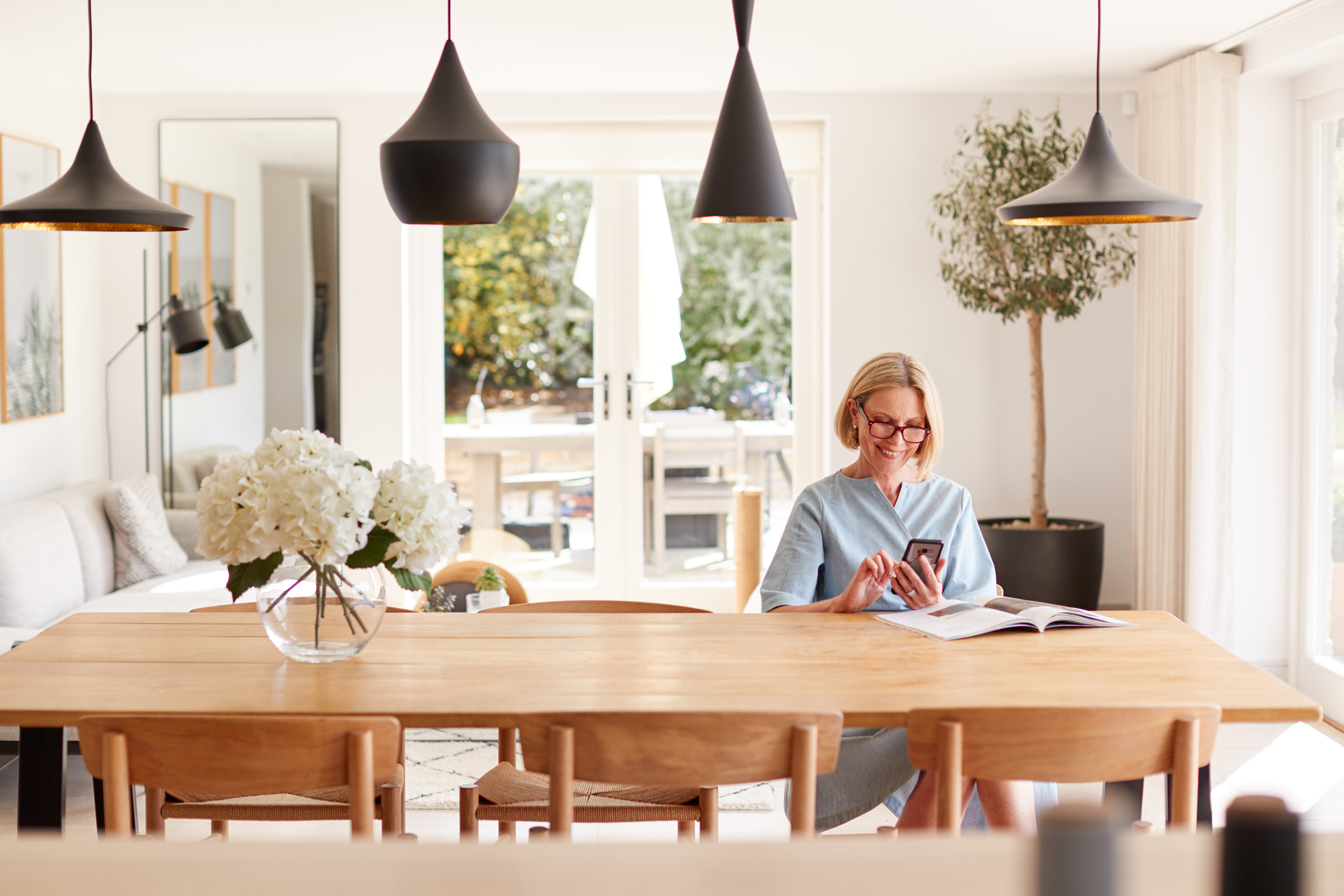 senior woman relaxing with magazine at home looking at phone