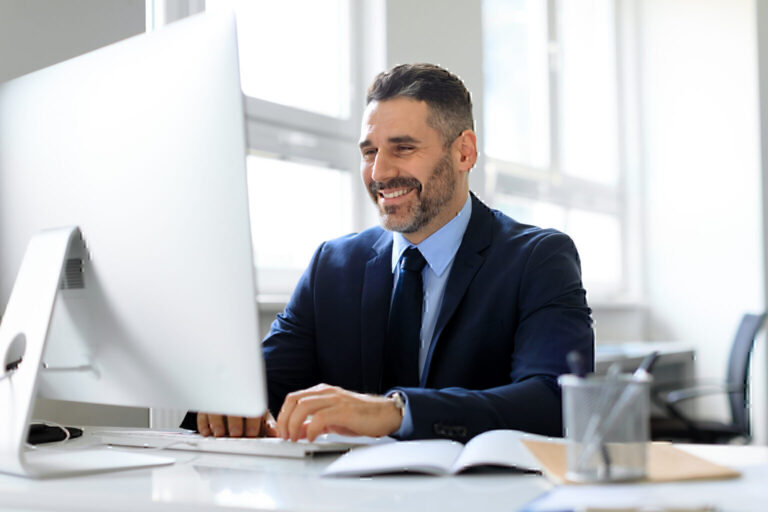 Smiling middle aged businessman in suit working on computer in office, checking email or chatting