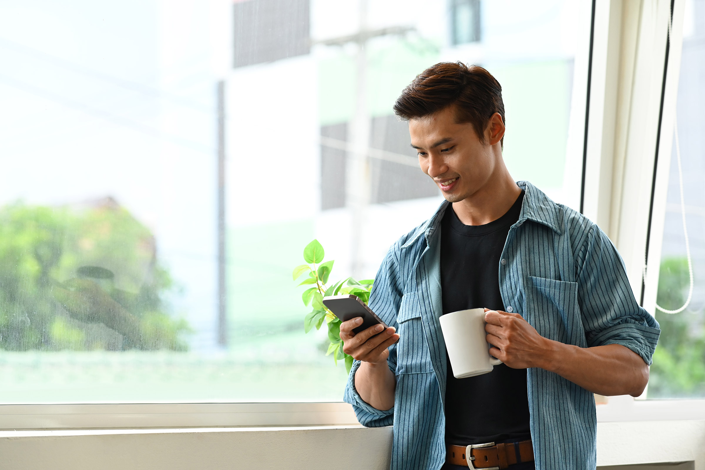 Smiling young Asian man drinking coffee and checking his phone