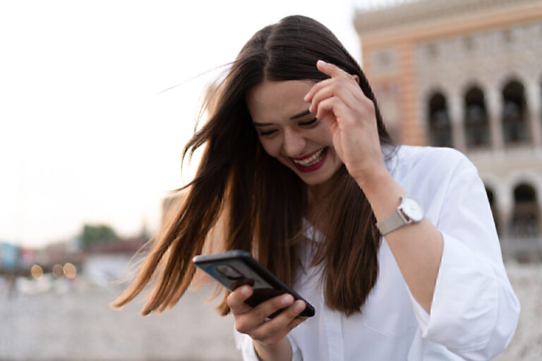 The young pretty woman writes and laughs on the cell phone