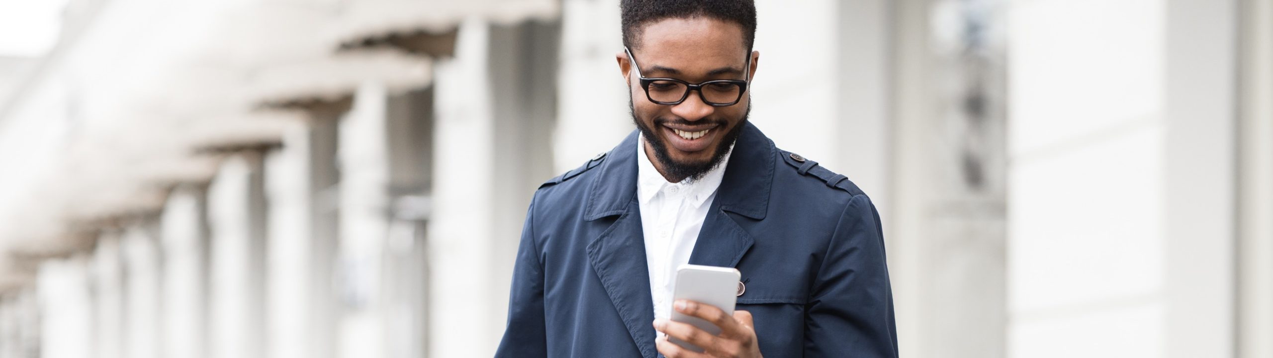 Young Black man texting on phone and standing with bike on city street.