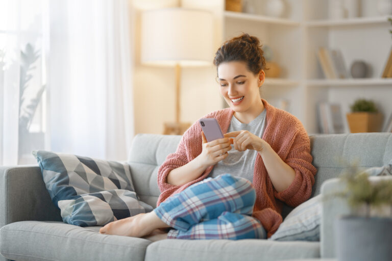 woman is using a phone sitting on a sofa