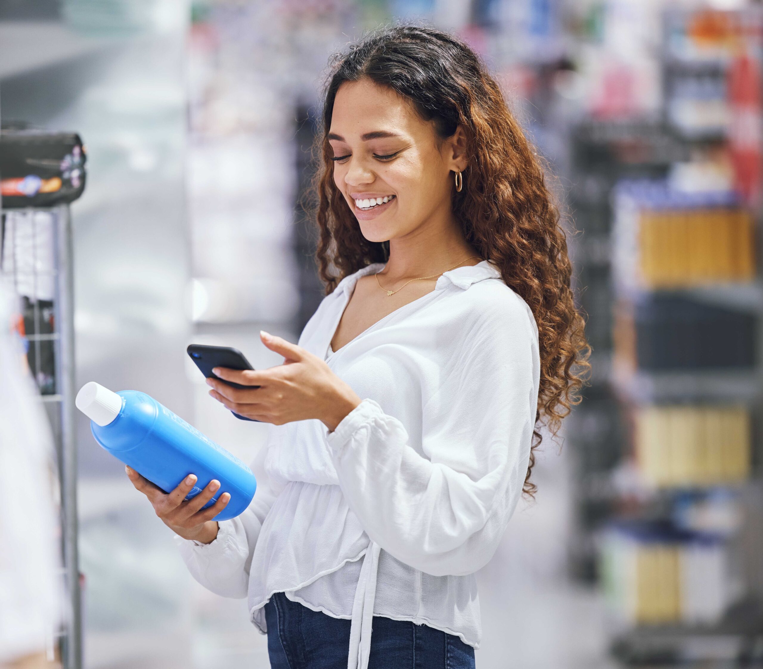 A woman in a retail store holding a water bottle while checking her phone.