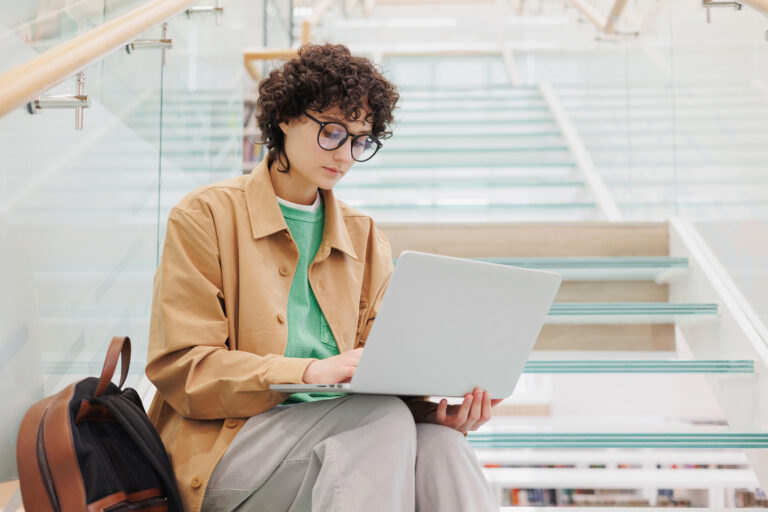 woman with curly hair is sitting on steps and working