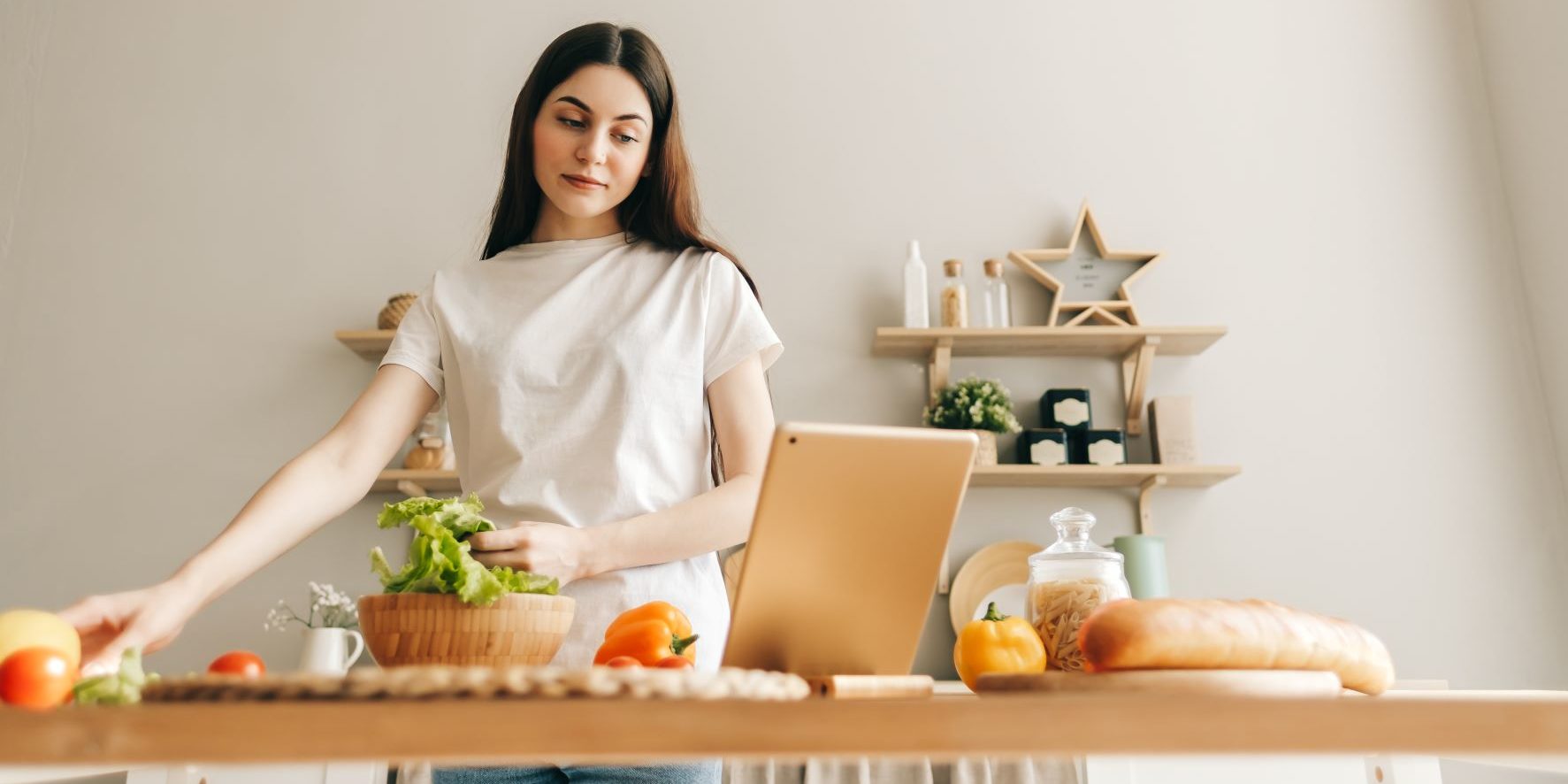 A woman prepares to cook at home while look at a tablet device propped up on the table.