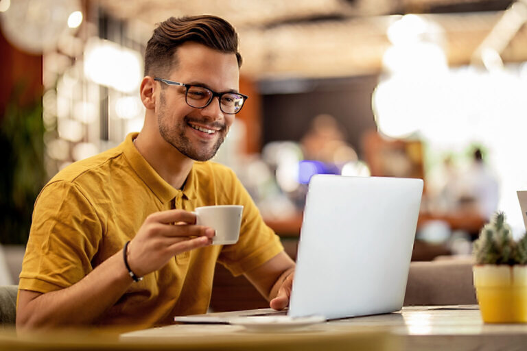 Young happy man using laptop and drinking coffee in a cafe.