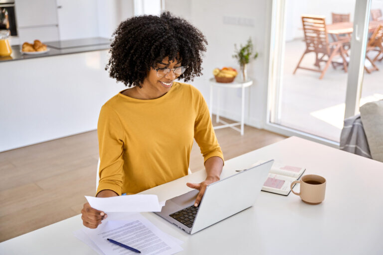 Young smiling happy African woman checking paper paying bills online at home.