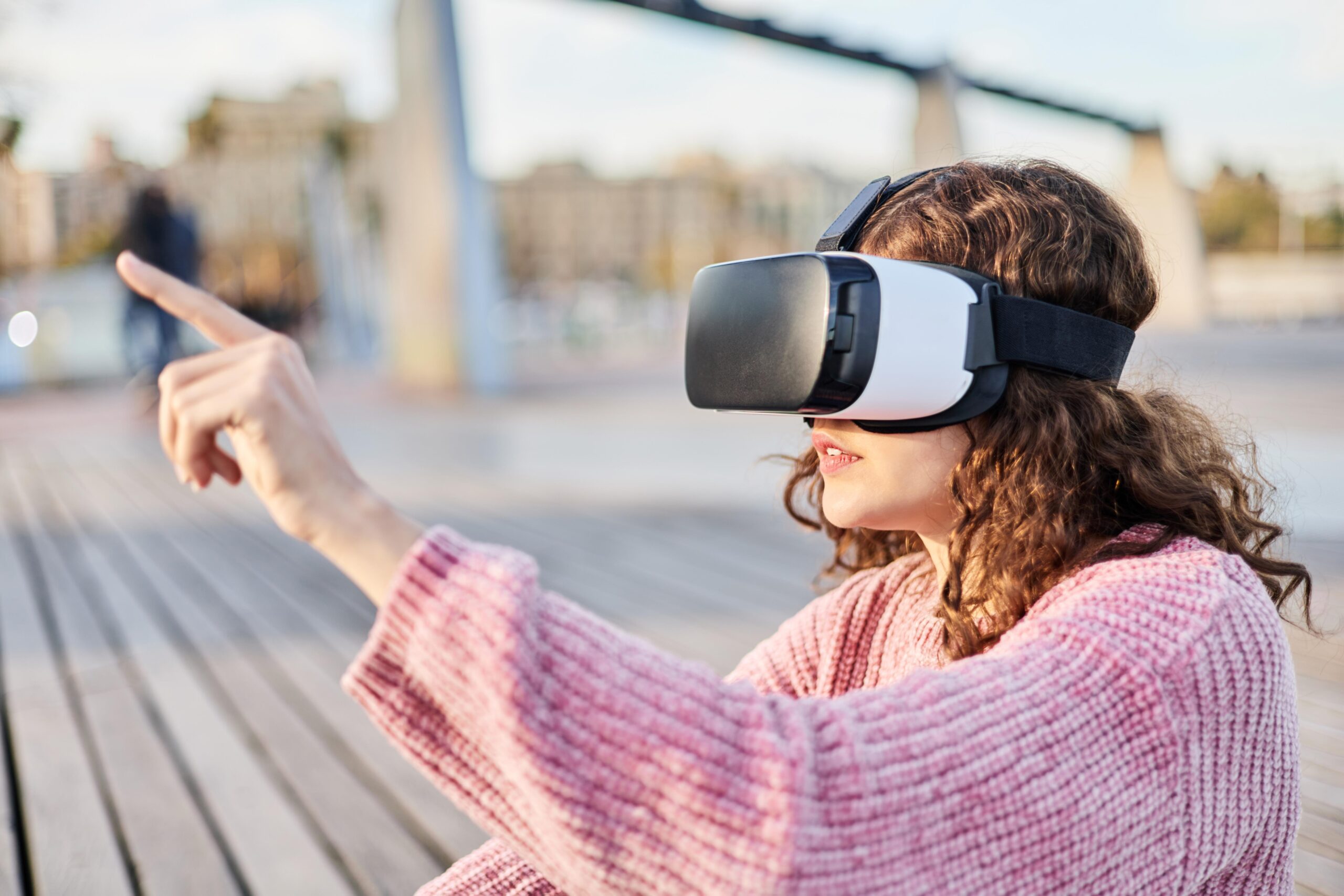 A young woman reaches out to a virtual object while wearing a VR headset outdoors