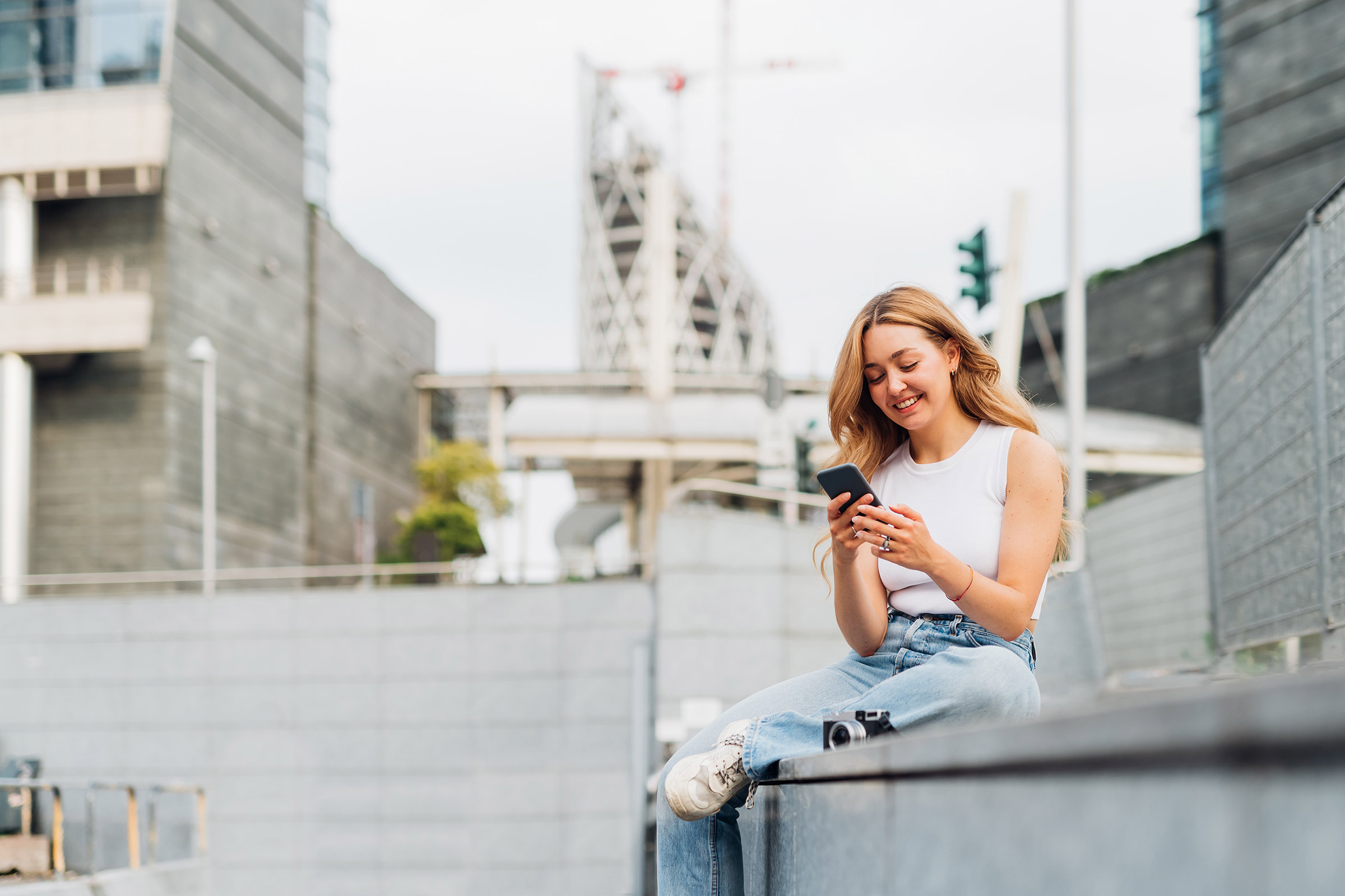 A young woman sits outdoors using her phone.
