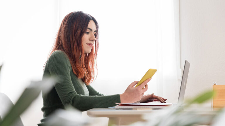 Young woman using smartphone and laptop
